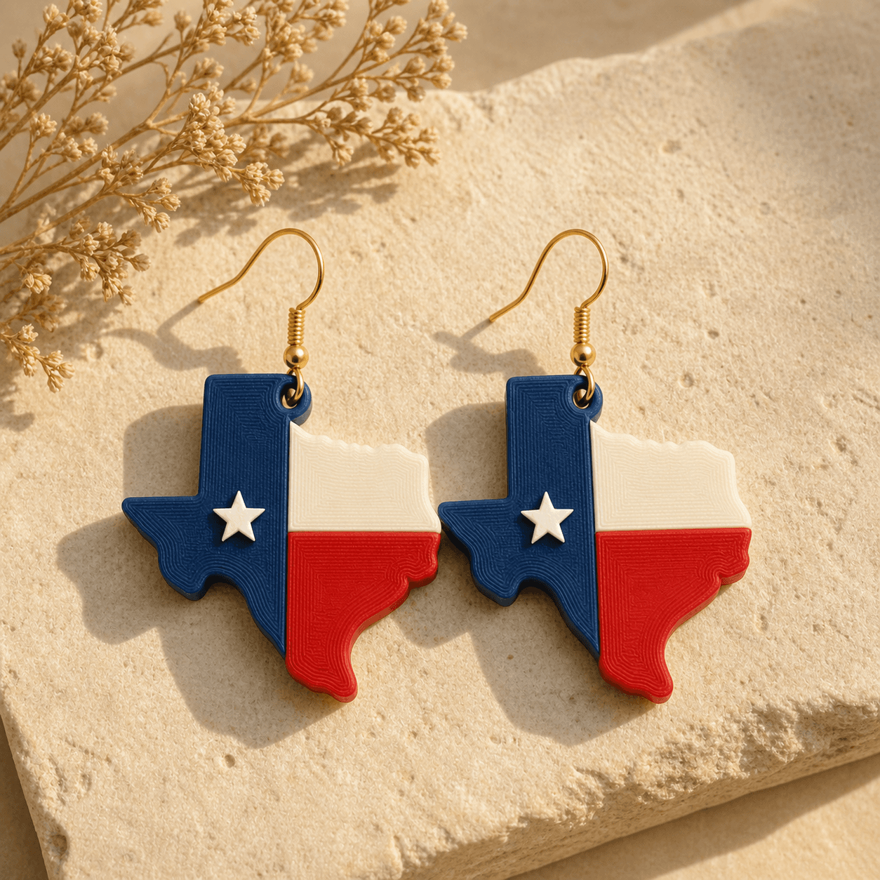 Red, White & Blue Texas Earrings laid on warm limestone with dried florals, showing the contoured print texture and raised star